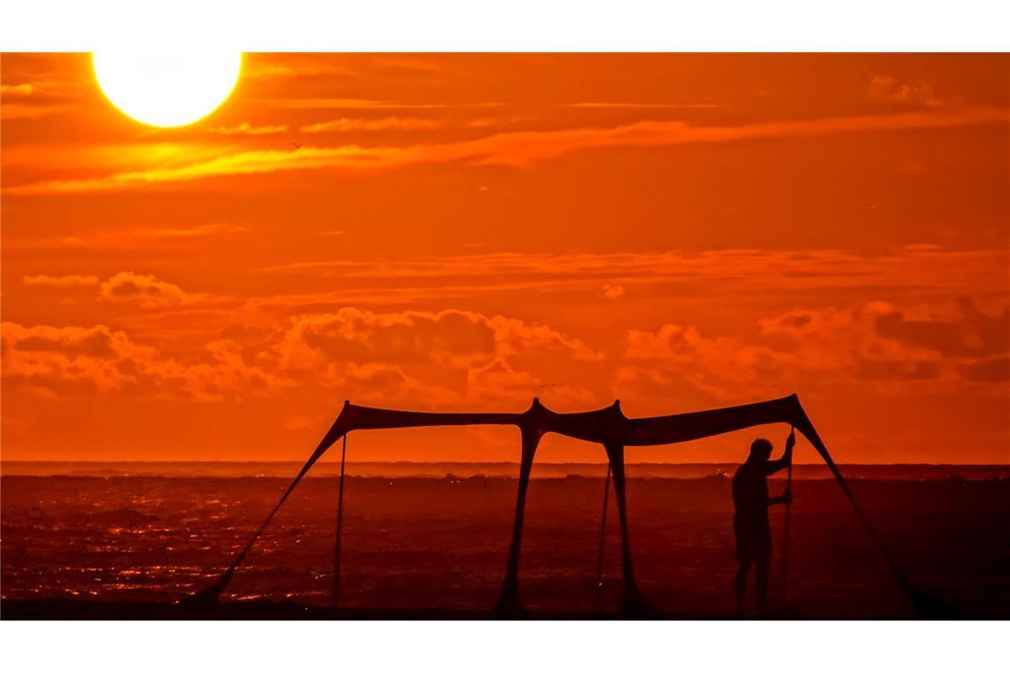 Hitze in den USA: Ein Strandbesucher baut im Schatten des Sonnenaufgangs einen Sonnenschirm am Strand von Wild Dunes auf in Isle of Palms, South Carolina.