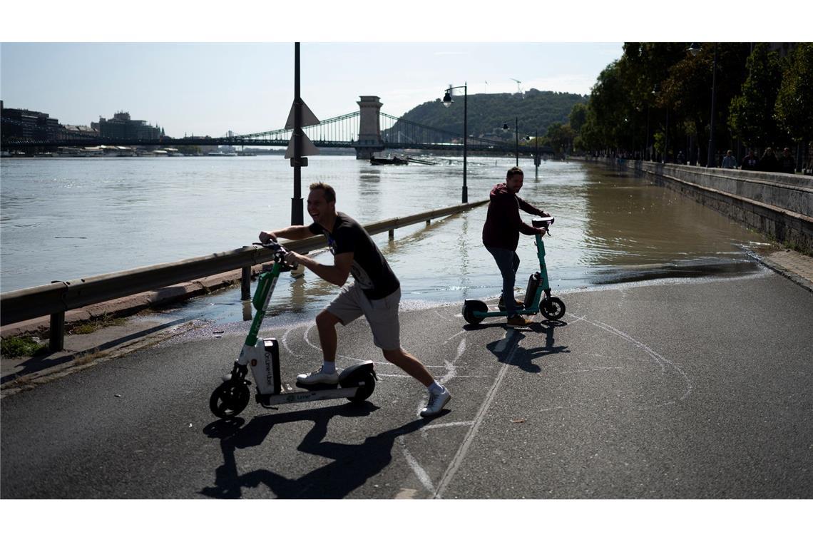 Hochwasser in Ungarn: Menschen fahren mit ihren Elektrorollern zu einer überschwemmten Straße.