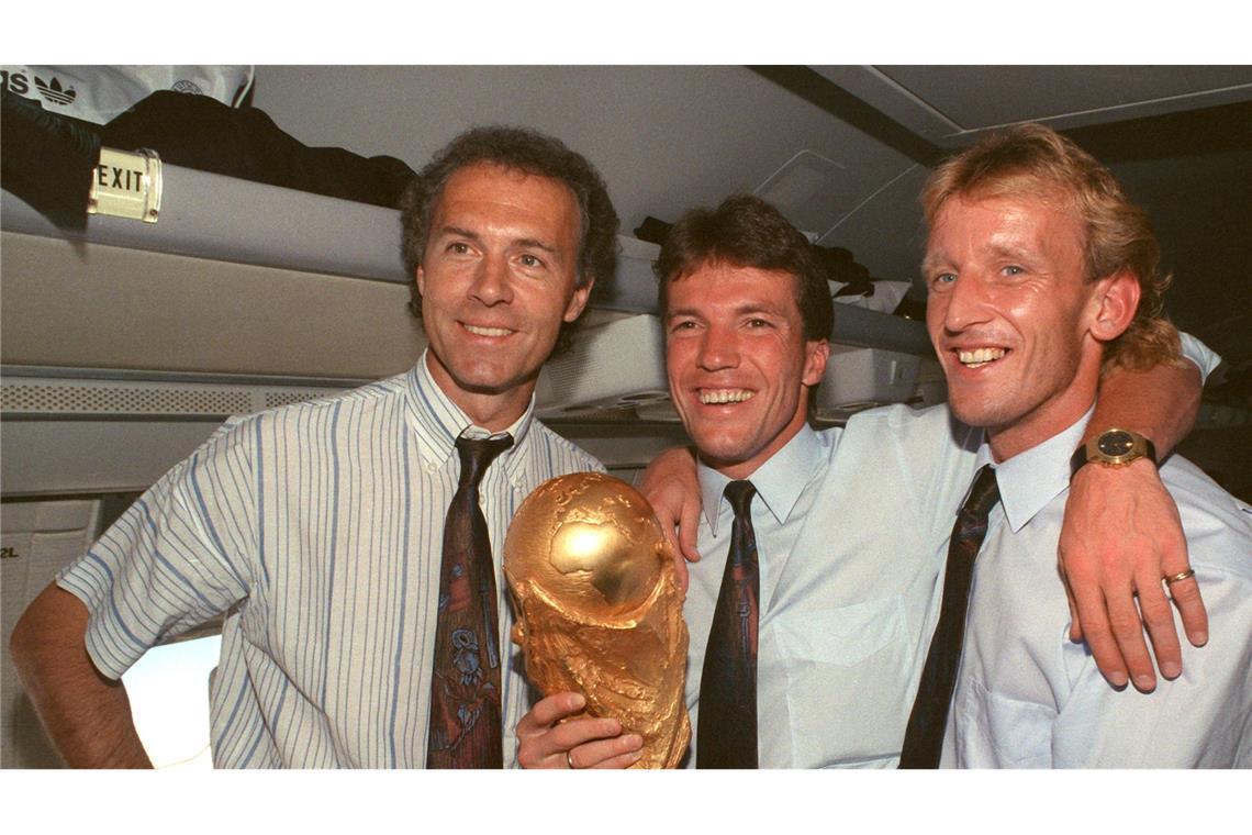 Im Flugzeug präsentieren der damalige DFB-Teamchef Franz Beckenbauer (l), Lothar Matthäus (M) und Andreas Brehme den WM-Pokal.