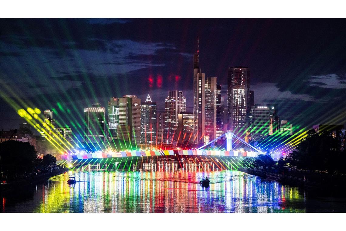 Im Vorfeld der bevorstehenden Fußball-EM ist die Flößerbrücke über den Main vor der Skyline von Frankfurt bei einer Lichtshow bunt illuminiert.