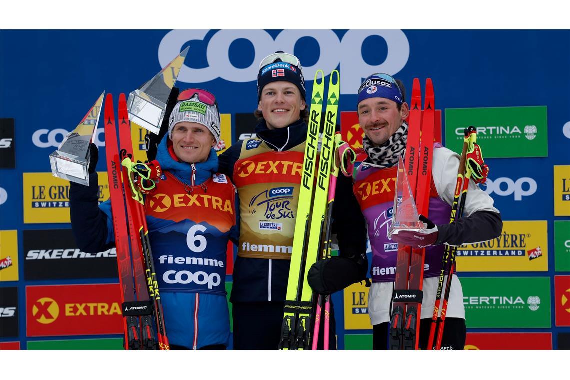 Johannes Hoesflot Klaebo (M) aus Norwegen jubelt neben dem Zweitplatzierten Mika Vermeulen (l) aus Österreich und dem Drittplatzierten Hugo Lapalus aus Frankreich auf dem Podium der Tour de Ski.