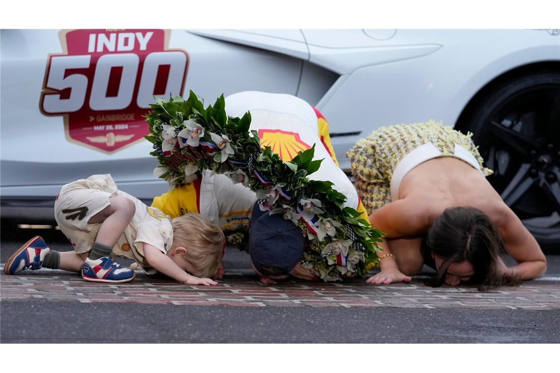 Josef Newgarden (M.) küsst gemeinsam  mit seinem Sohn Kota und seiner Frau Ashley Welch den Boden, nachdem er das Indianapolis 500 Autorennen auf dem Indianapolis Motor Speedway gewonnen hat.