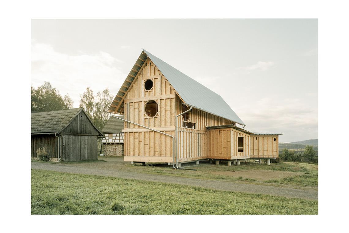 Jun. Pro. Max Otto Zitzelsberger aus Kaiserslautern: Lernhaus für Umweltbildung in Nabburg in Bayern. Das neue museumspädagogische Gebäude steht auf dem Gelände des Freilandmuseums Oberpfalz. Es handelt sich um einen einfachen Holzständerbau. Das Holz stammt aus dem nahe gelegenen Wald, wurde im Winter geschlagen, sorgfältig vor Ort mit einer mobilen Säge geschnitten und ein Jahr lang behutsam getrocknet. Materialien werden so sparsam wie möglich eingesetzt. So konnten beispielsweise auf Grund der hohen Qualität die Querschnitte der tragenden Kanthölzer reduziert werden. Das Gebäude wurde aufgeständert und sitzt auf wenigen betonierten Fundamenthälsen. Damit ließ sich die notwendige Menge an Beton auf ein Minimum begrenzen.