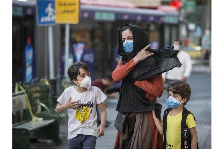 Kinder mit Gesichtsmasken gehen mit ihrer Mutter eine Straße entlang in Teheran. Der Iran hat nun Bußgelder bei Verstößen gegen die Corona-Regeln eingeführt. Foto: Ahmad Halabisaz/XinHua/dpa