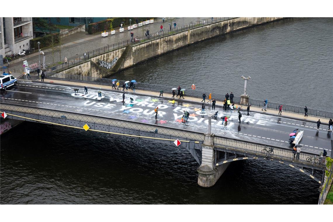 Klimaaktivisten der Bewegung Fridays for Future malen auf der Marschallbrücke in Berlin den Schriftzug "Our world is on fire - use your voice!".