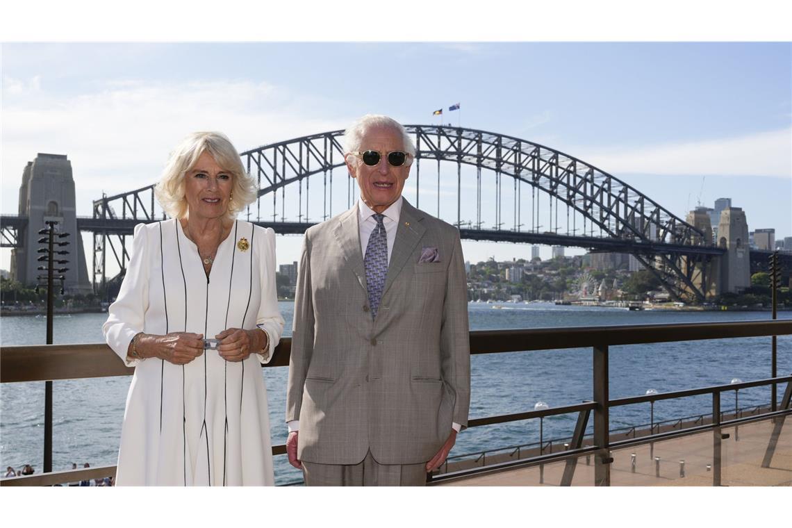 König Charles III. und Königin Camilla stehen auf einer Empore des Opernhauses, hinter ihnen ist die Sydney Harbour Bridge zu sehen.