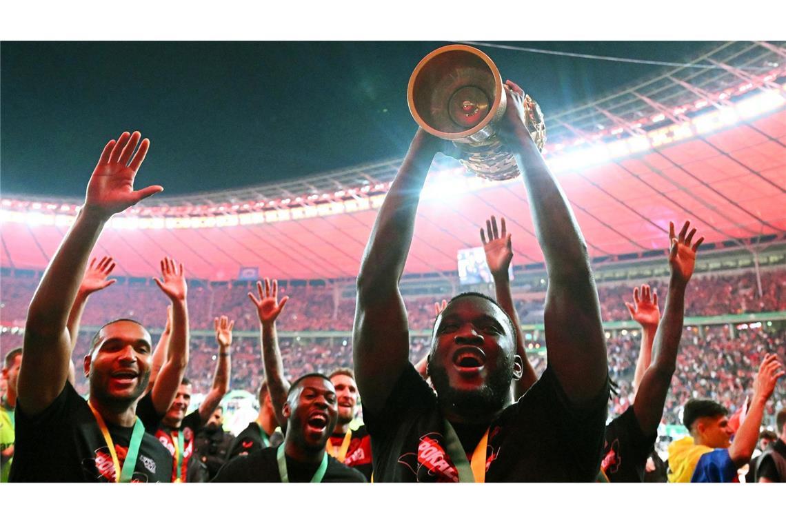 Leverkusens Victor Boniface (r) hält den Pokal jubelnd hoch, während seine Teamkollegen feiern.