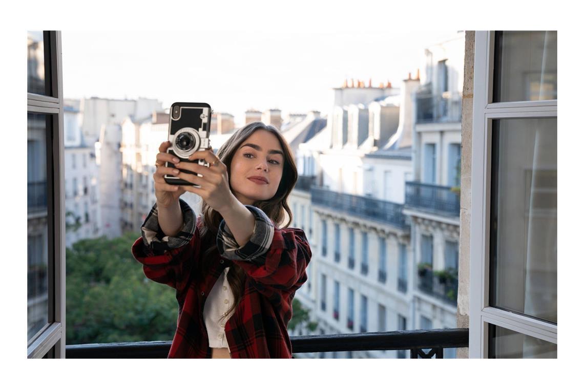 Lily Collins als Titelfigur der Serie „Emily in Paris“, die in dieser Szene vor allem an sich interessiert scheint. Seit 2020 spielt sie in der Netflix-Serie „Emily in Paris“ die Hauptrolle – neben der architektonischen Superdiva namens Paris.