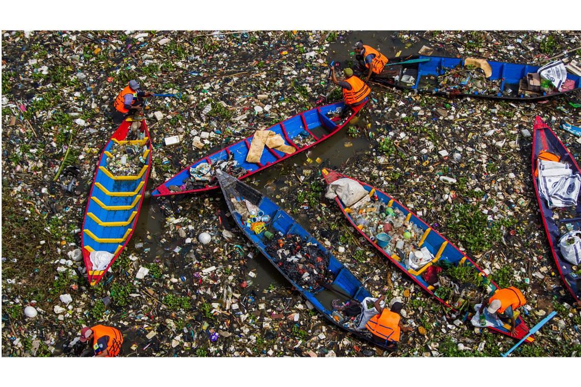 Männer säubern mit einem Holzboot den Citarum-Fluss im indonesischen Bandung von Plastikmüll, der sich dort angesammelt hat.