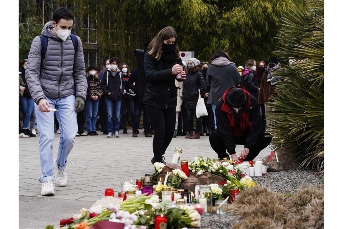 Menschen legen vor einem Gebäude der Universität Blumen und Kerzen an den Wegesrand. Foto: Uwe Anspach/dpa