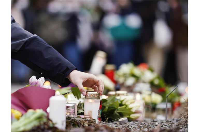 Menschen legen vor einem Gebäude der Universität Blumen und Kerzen an den Wegesrand. Foto: Uwe Anspach/dpa/Archivbild