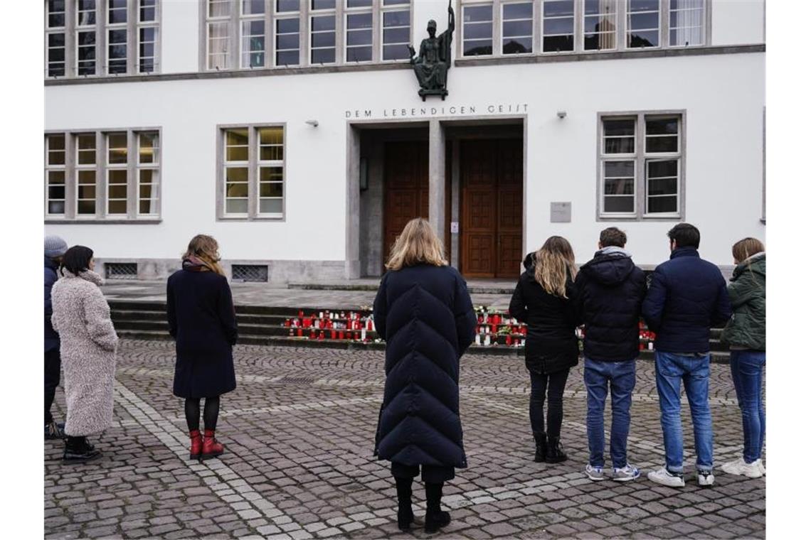 Menschen stehen zur Gedenkminute vor dem Haupteingang der Neuen Universität. Foto: Uwe Anspach/dpa