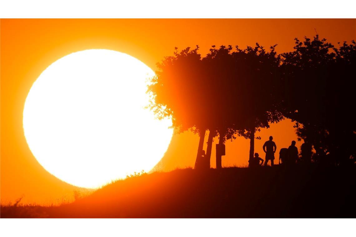 Menschen verweilen auf dem Kronsberg, während am Horizont die Sonne untergeht.