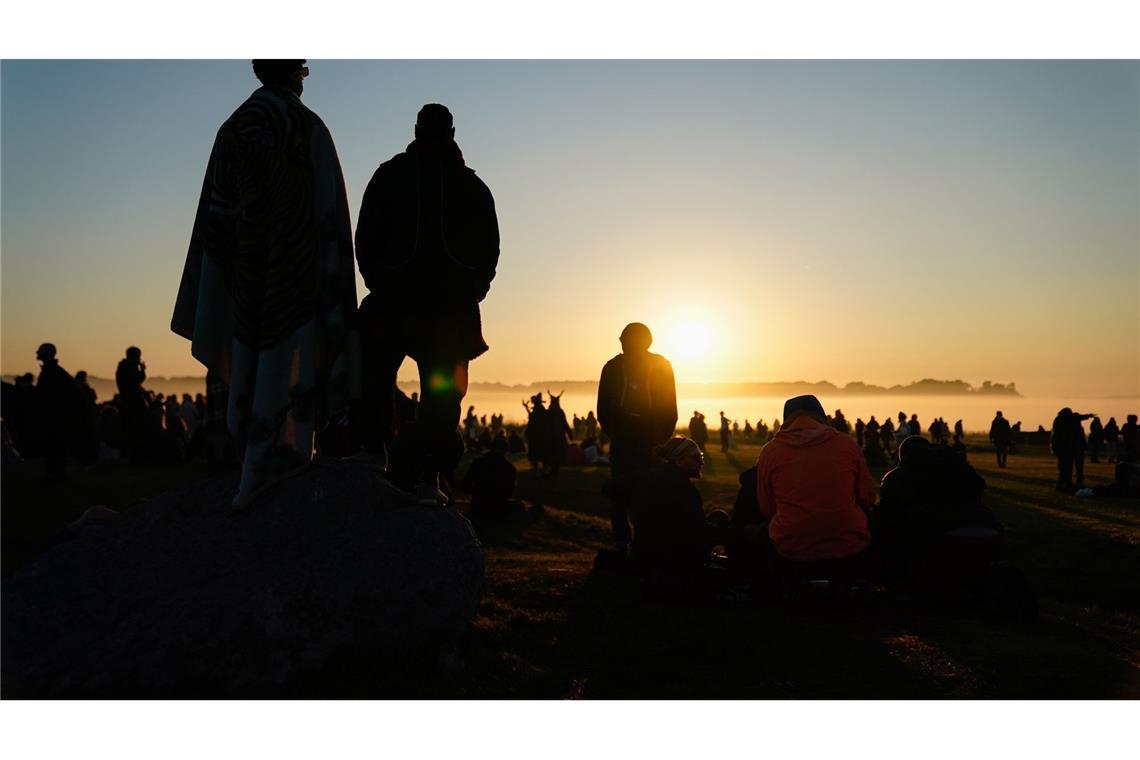 Menschen während des Sonnenaufgangs im britischen Wiltshire - sie nehmen an der mystischen Sommersonnenwende in Stonehenge teil.