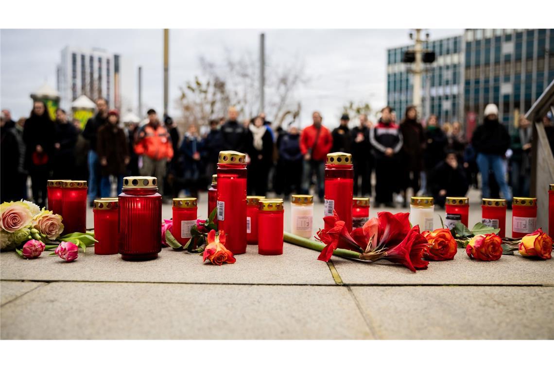 Menschen zünden Kerzen an und legen Blumen nieder.