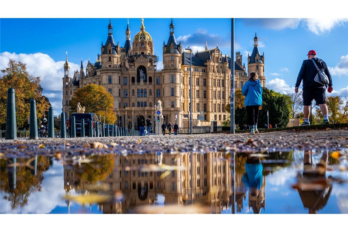 Milder Herbst: Schweriner Schloss spiegelt sich in einer Pfütze.