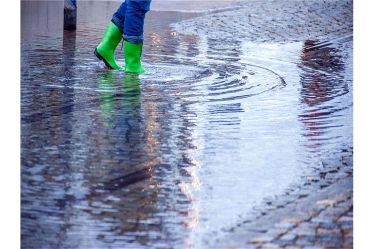 Mit Gummistiefeln geht eine Frau über eine leicht überflutete Straße. Foto: Jens Büttner/dpa-Zentralbild/dpa/Symbolbild