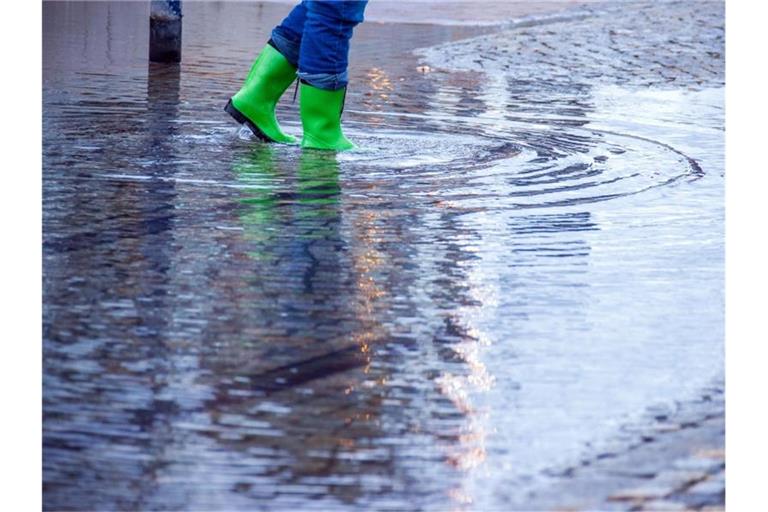 Mit Gummistiefeln geht eine Frau über eine leicht überflutete Straße. Foto: Jens Büttner/dpa-Zentralbild/dpa/Symbolbild