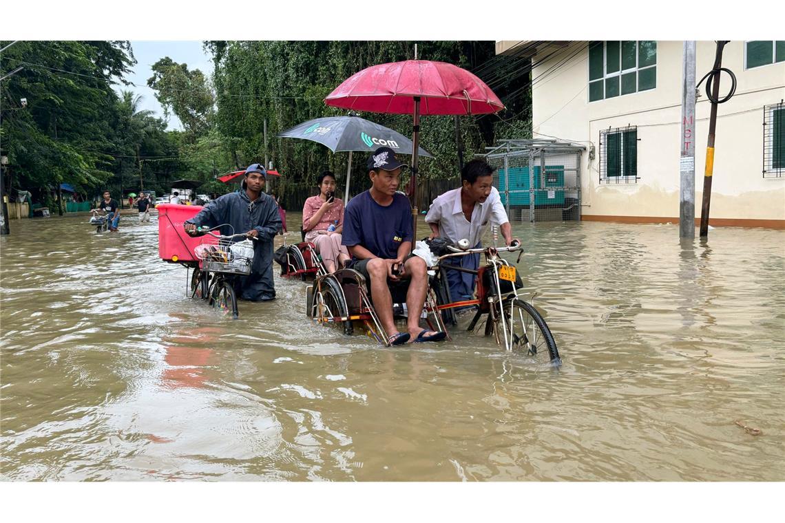 Mit Hilfe von Trishaws und Fahrräder bahnen sich Menschen ihren Weg durch eine überflutete Straße Myanmar.