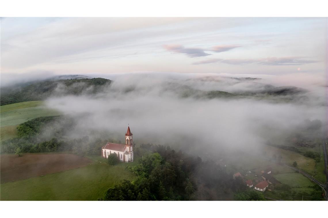 Morgennebel steigt über der Herz-Jesu-Kirche im ungarischen Soshartyan auf.