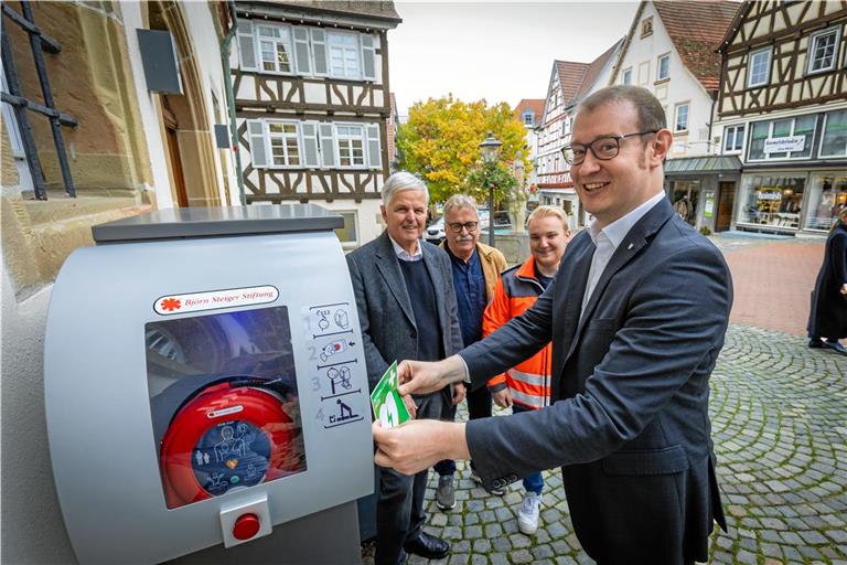 Oberbürgermeister Maximilian Friedrich klebt einen Hinweissticker auf den neuen Defibrillator, der am Briefkasten vor dem historischen Rathaus in Backnang installiert wurde. Im Hintergrund (von links): Bernhard Weber, Klaus Böhle und Cedric Caspari. Foto: Alexander Becher