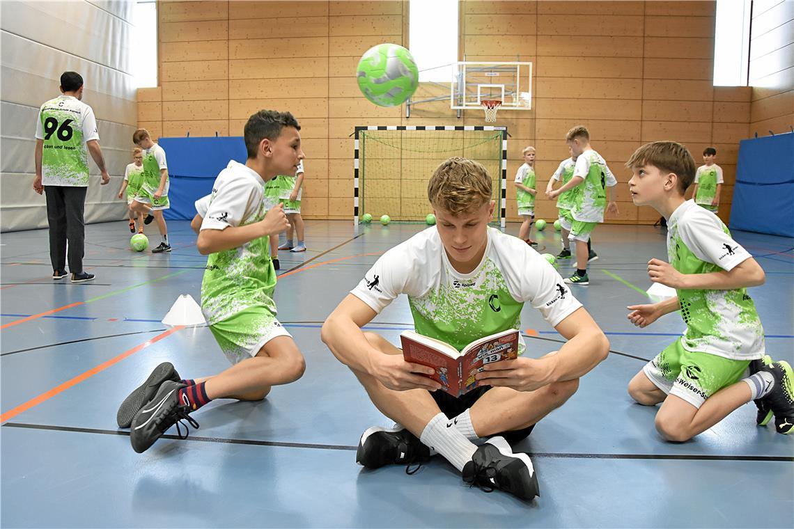 Oberliga-Kicker Nico Engel (mit Buch) und Lehrkraft Tolga Durmaz (Trikotnummer 96) üben mit den Schülern der Großaspacher Conrad-Weiser-Schule in der Mühlfeldhalle Aspach. Foto: Tobias Sellmaier