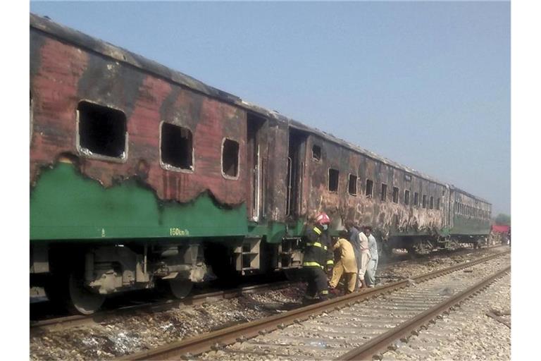 Pakistanische Beamte untersuchen den Zug nach dem Brand. Foto: Siddique Baluch/AP/dpa