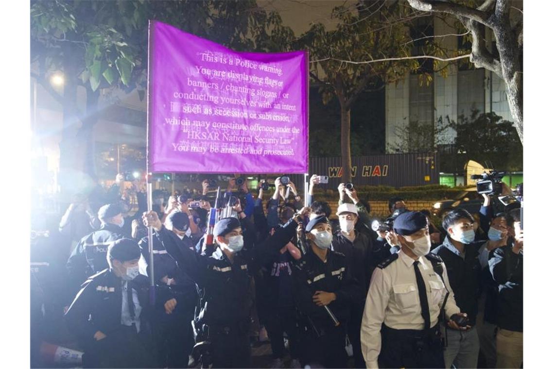 Sicherheitsgesetz: 47 Hongkonger Aktivisten müssen in U-Haft Polizisten hissen vor einem Gericht in Hongkong eine Warnflagge gegen die Unterstützer von 47 pro-demokratischen Aktivisten, die wegen angeblicher Verstöße gegen das neue Sicherheitsgesetz vorerst in Untersuchungshaft bleiben müssen. Foto: Vincent Yu/AP/dpa