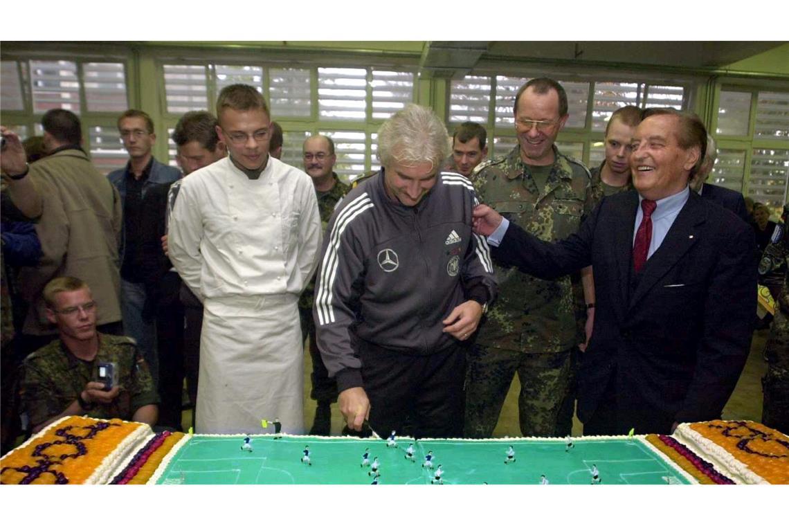 Rudi Völler (M) schneidet beim Truppenbesuch in Sarajevo eine Torte in Form eines Fußallplatzes an.