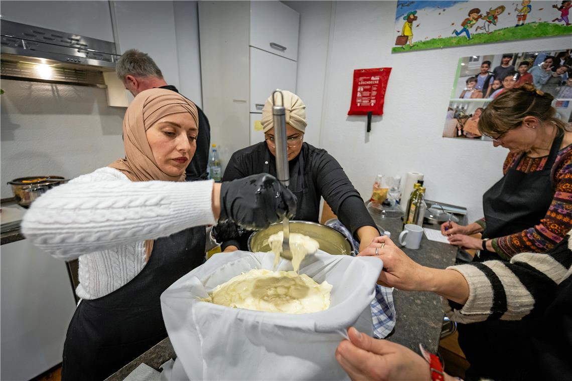 Safaa Ezzedinne aus Syrien schöpft die Masse aus dem Topf von Ines Loubiri in ein Siebtuch zur Weiterverarbeitung. Foto: Alexander Becher