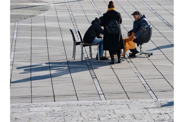 Schachspieler sitzen an einem Tisch auf dem Schlossplatz in der Sonne. Foto: Bernd Weißbrod/dpa