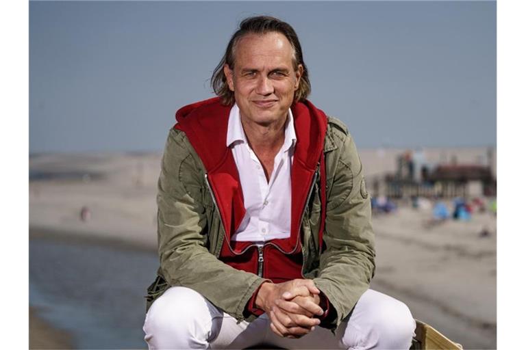 Schauspieler und Filmemacher Ralf Bauer sitzt am Strand von St. Peter Ording in der Sonne. Foto: Axel Heimken/dpa/Archivbild