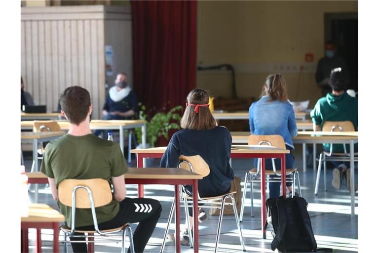 Schüler mit Mundschutz sitzen bei der Prüfungsvorbereitung fürs Abitur in einer zum Schulraum umfunktionierten Turnhalle. Foto: Bodo Schackow/dpa-Zentralbild/dpa/Archivbild