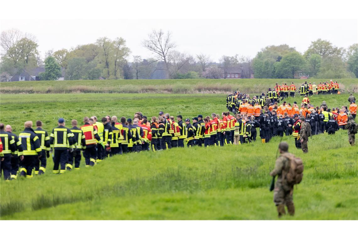 Soldaten der Bundeswehr und Einsatzkräfte von Feuerwehr und Polizei stellen sich auf, um ein Feld abzusuchen.