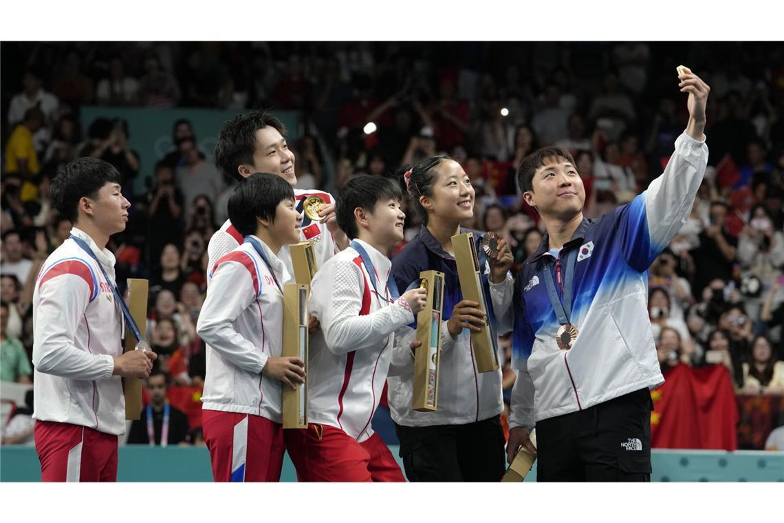 Südkoreas Lim Jonghoon (r) mit dem Smartphone in der Hand bei der Siegerehrung, die Olympiasieger Wang Chuqin und Sun Yingsha aus China (M), feiern mit den Zweitplatzierten Kim Kum Yong und Ri Jong Sik aus Nordkorea (l) und den Dritten Shin Yubin/Lim Jonghoon aus Südkorea.