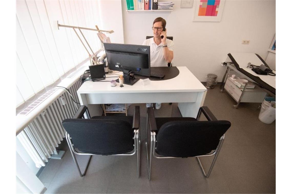 Thomas Heyer sitzt in seiner Hausarztpraxis mit einem Telefonhörer am Ohr in einem Behandlungszimmer. Foto: Marijan Murat/dpa