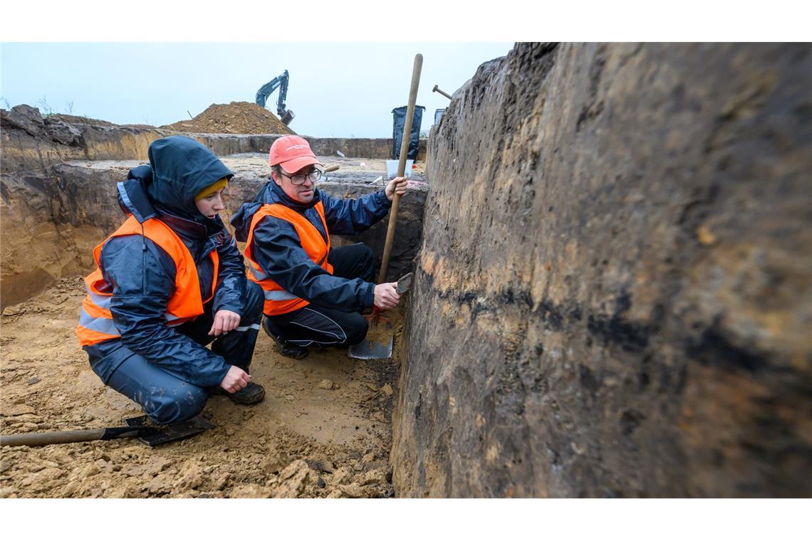 Thomas Lukas, Grabungsleiter des Landesamtes für Archäologie Sachsen, betrachtet mit einer Studentin  Verfärbungen durch Holzkohle und Brandlehm einer mehrschichtigen Grubenverfüllung auf einem Grabungsfeld bei Döbeln.