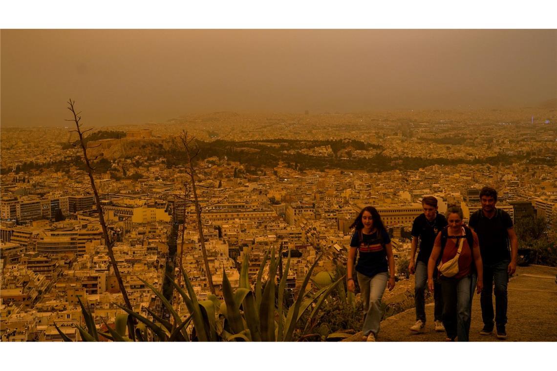 Touristen spazieren auf dem Lycabettus-Hügel, während der Himmel über Athen mit dem antiken Akropolis-Hügel im Hintergrund infolge von Saharastaub eingetrübt ist.