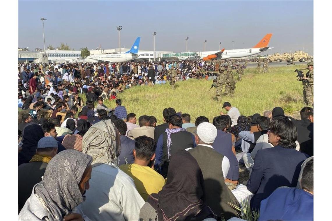 US-Soldaten bewachen eine Absperrung am Flughafen in Kabul, dahinter sitzen und stehen Afghanen und Afghaninnen. Foto: -/AP/dpa/Archivbild