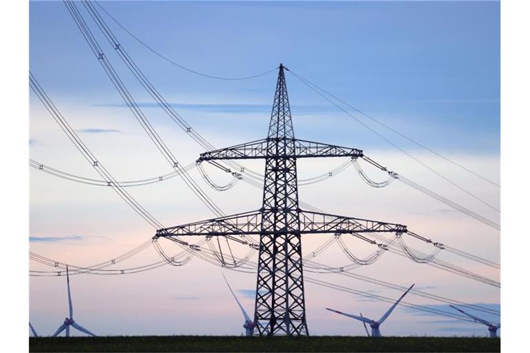 Windräder stehen hinter dem Mast einer Stromtrasse. Foto: Karl-Josef Hildenbrand/dpa/Symbolbild