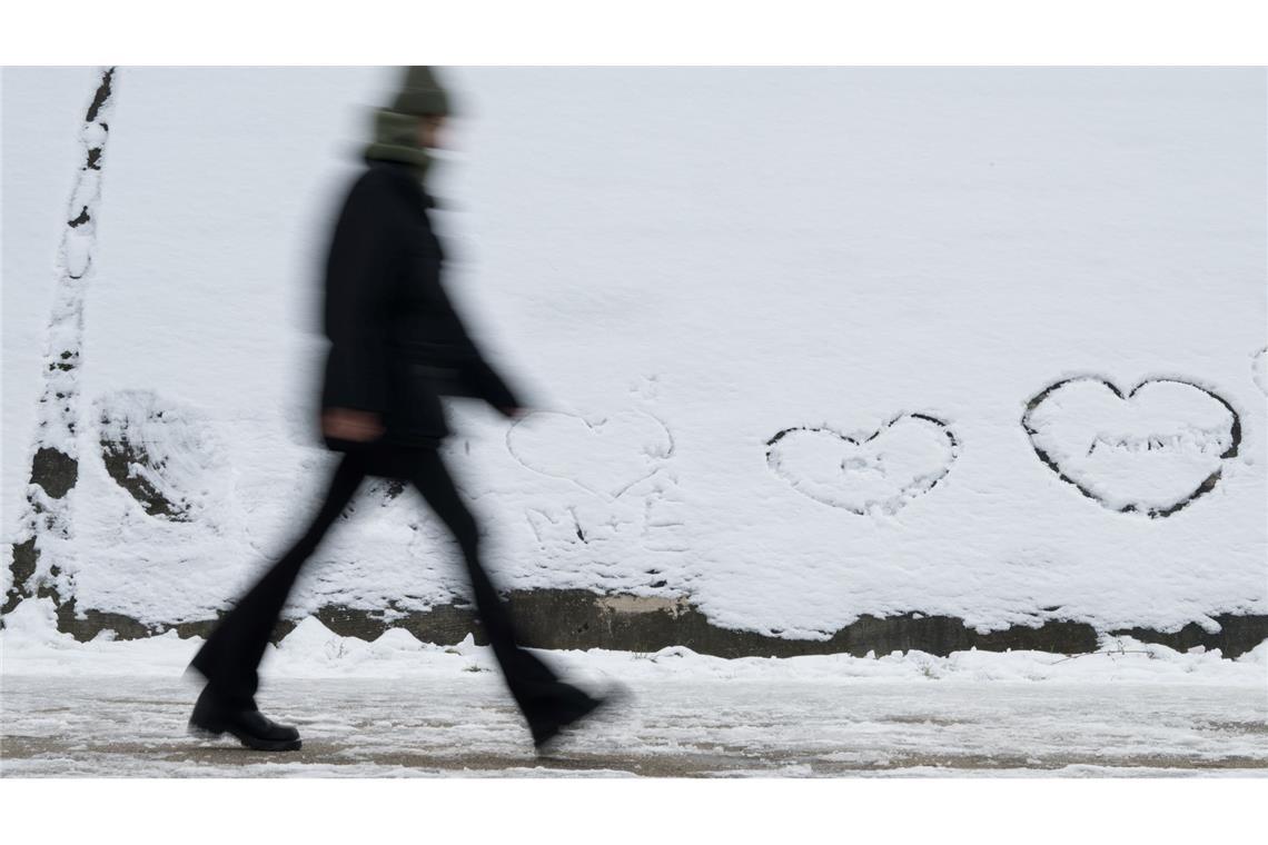 Winterwetter in Berlin: Eine Person geht an einer Wand vorbei, auf der im Schnee Herzen geschrieben sind.