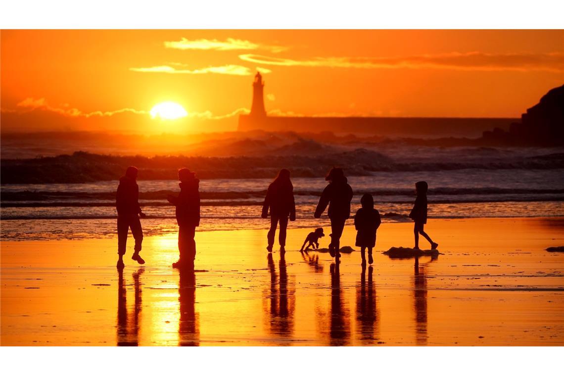 Winterwetter in Großbritannien: Spaziergänger gehen bei Sonnenaufgang am Strand von Tynemouth