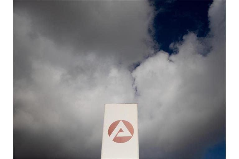 Wolken ziehen über ein Schild der Agentur für Arbeit. Foto: Carsten Koall/dpa/Symbolbild