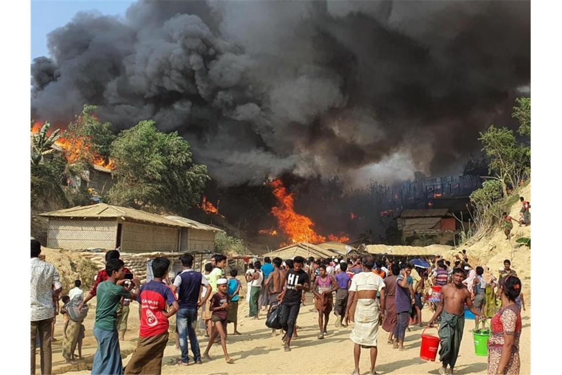 Bangladesch: Tote bei Brand in Flüchtlingslager für Rohingya Zahlreiche Menschen betrachten den Rauch, der über dem in Flammen stehenden Lager aufsteigt. Foto: Shafiqur Rahman/AP/dpa