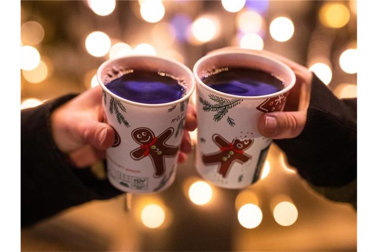 Zwei Besucherinnen eines Weihnachtsmarktes stoßen mit Glühwein an. Foto: Christoph Schmidt/dpa/Symbolbild