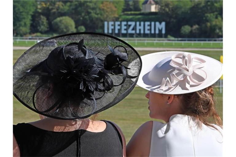 Zwei Frauen mit Hüten gucken bei der Großen Woche auf die Galopprennbahn Iffezheim. Foto: Uli Deck/dpa/archivbild