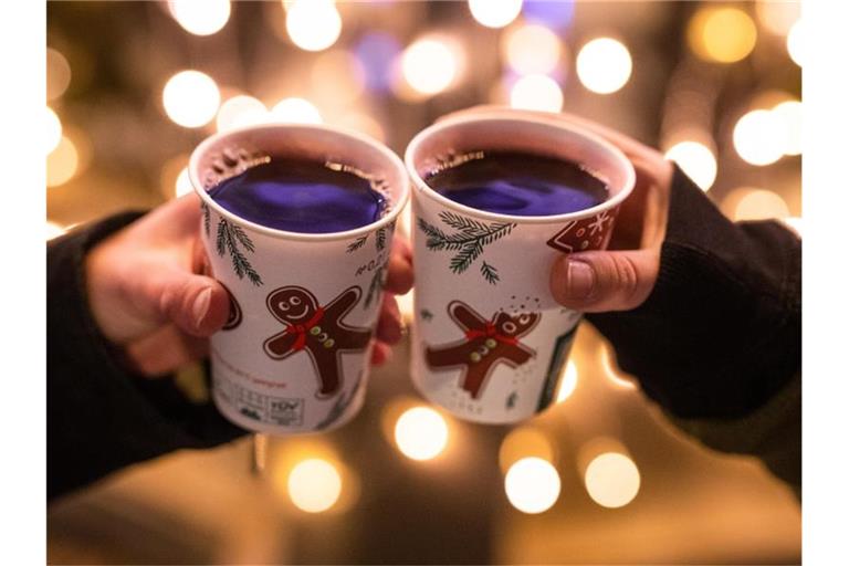 Zwei Frauen stoßen mit Glühwein in Bechern auf dem Weihnachtsmarkt an. Foto: Christoph Schmidt/dpa