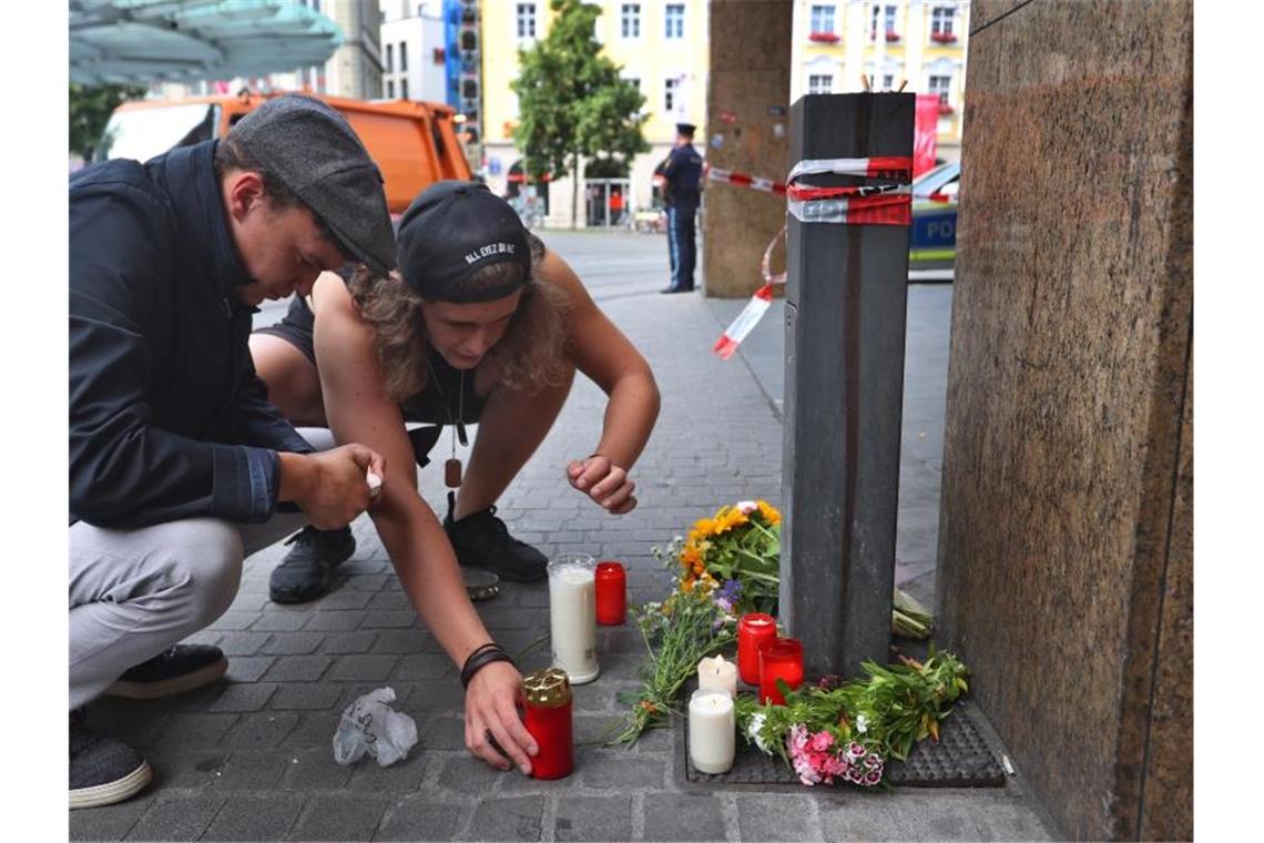 Zwei junge Männer entzünden vor einem abgesperrten Geschäft in der Innenstadt eine Kerze. Foto: Karl-Josef Hildenbrand/dpa