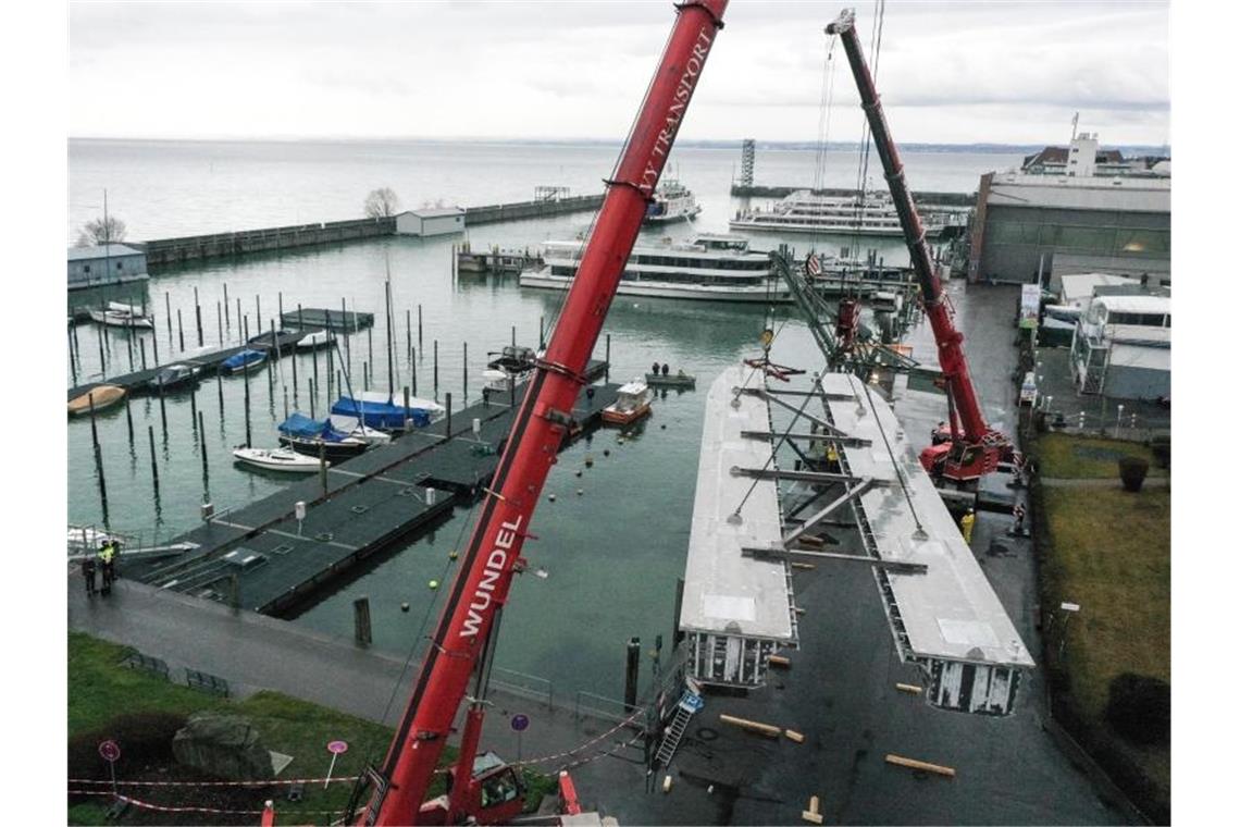 Teile für erste Elektrofähre am Bodensee eingetroffen Zwei Kräne hieven die beiden Rümpfe für den künftigen E-Katamaran vom Land ins Hafenbecken. Foto: Felix Kästle/dpa