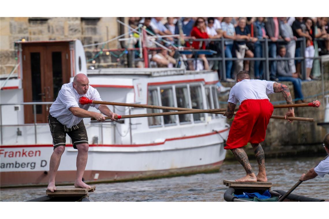 Zwei Männer versuchen sich beim 70. Fischerstechen in Bamberg gegenseitig mit langen Stöcken ins Wasser zu stoßen.